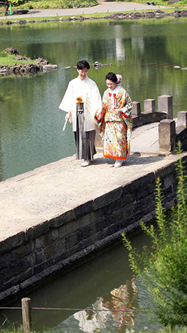 日本庭園にかかる橋を手を繋ぎ歩く新郎新婦