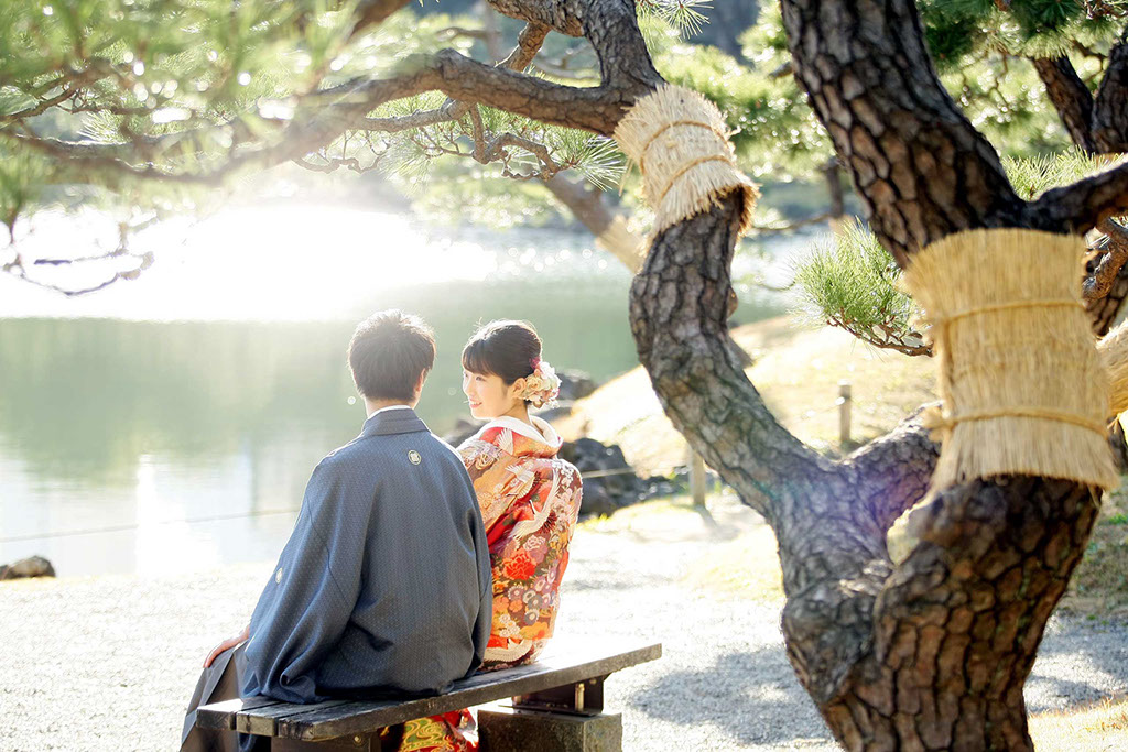 芝離宮の池のほとりに座り談笑する和装姿の新郎新婦