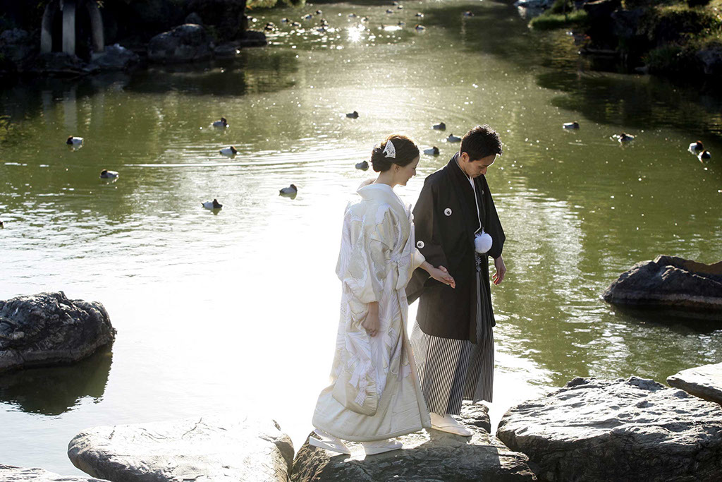 清澄庭園の石橋を手を繋いで渡る和装姿の新郎新婦