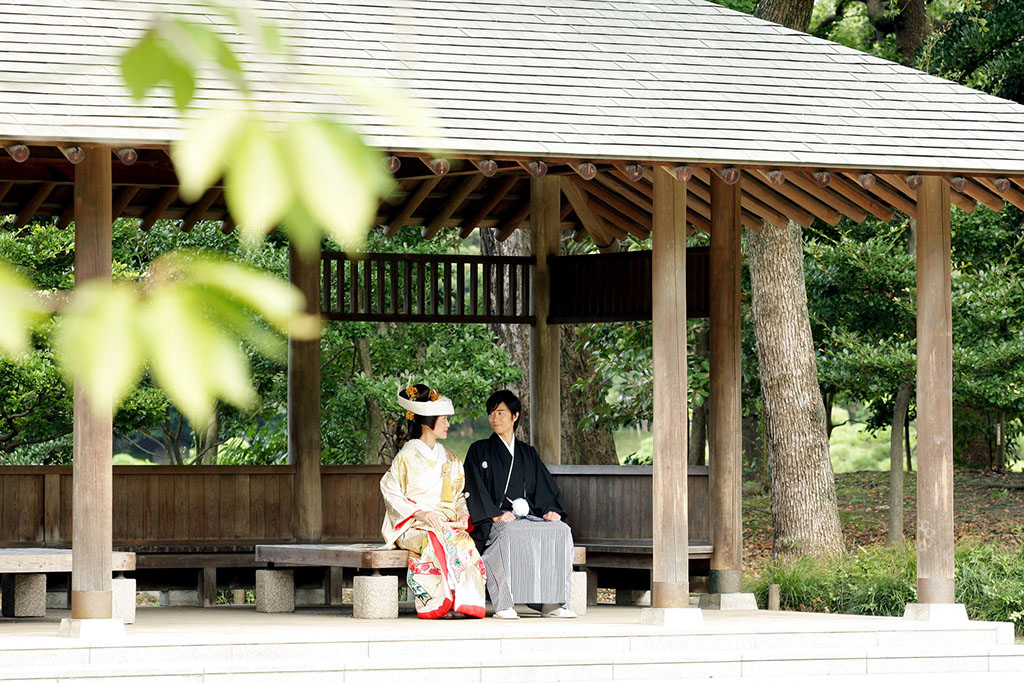 池のほとりの浮見堂でカメラを向きポーズをとる新郎新婦