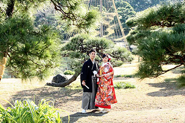 雪吊りの松の前に立つ和装姿の新郎新婦