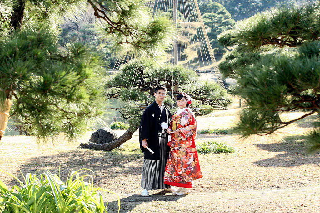 雪吊りの松の前に立つ和装姿の新郎新婦